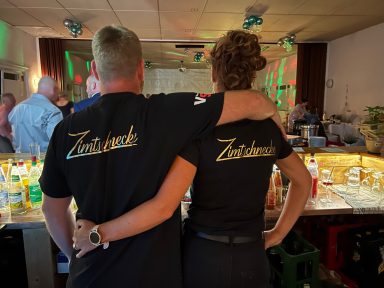 Zwei Personen mit schwarzen T-Shirts, die Rücken an Rücken stehen, in einer Bar.